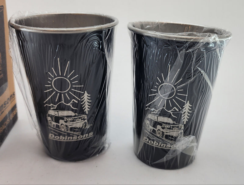 Two black cups with white designs on a white surface, with a cardboard box in the background.